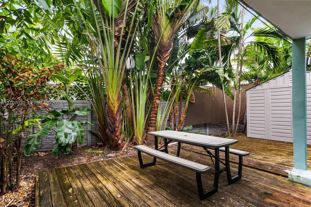 Outdoor deck with wood planks, mature tropical landscaping, and a masonry perimeter wall