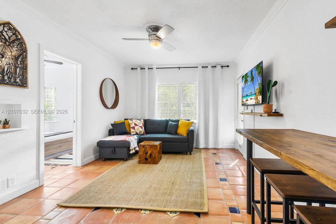 Terra-cotta tile flooring with decorative accent inlays, crown molding, built-in wall niche, and ceiling fan with integrated lighting