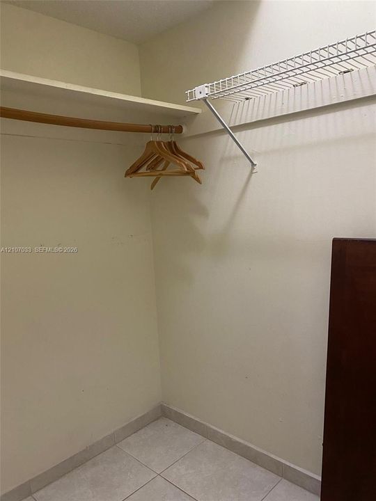 Storage space featuring a wooden garment rod, fixed shelving, a white wire rack, and tile flooring
