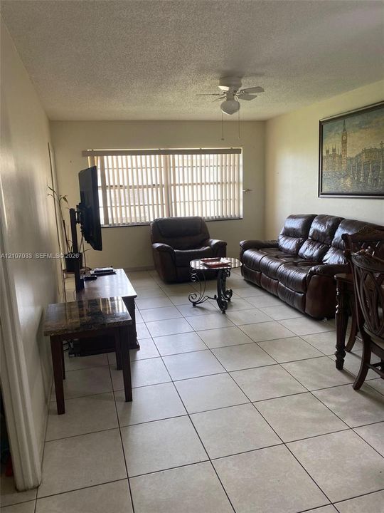 Interior space featuring neutral tile flooring, window with vertical blinds, and ceiling fan with integrated lighting