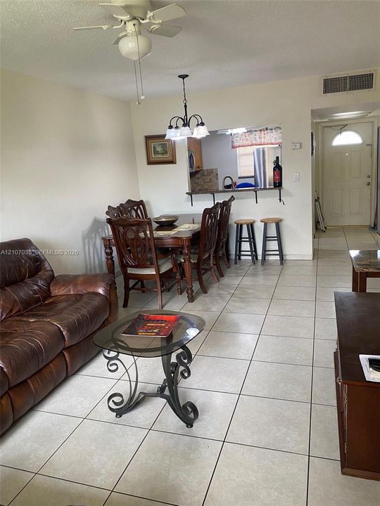 Light-toned ceramic tile flooring, neutral wall finishes, four-light chandelier, ceiling-mounted fan, and a kitchen pass-through counter