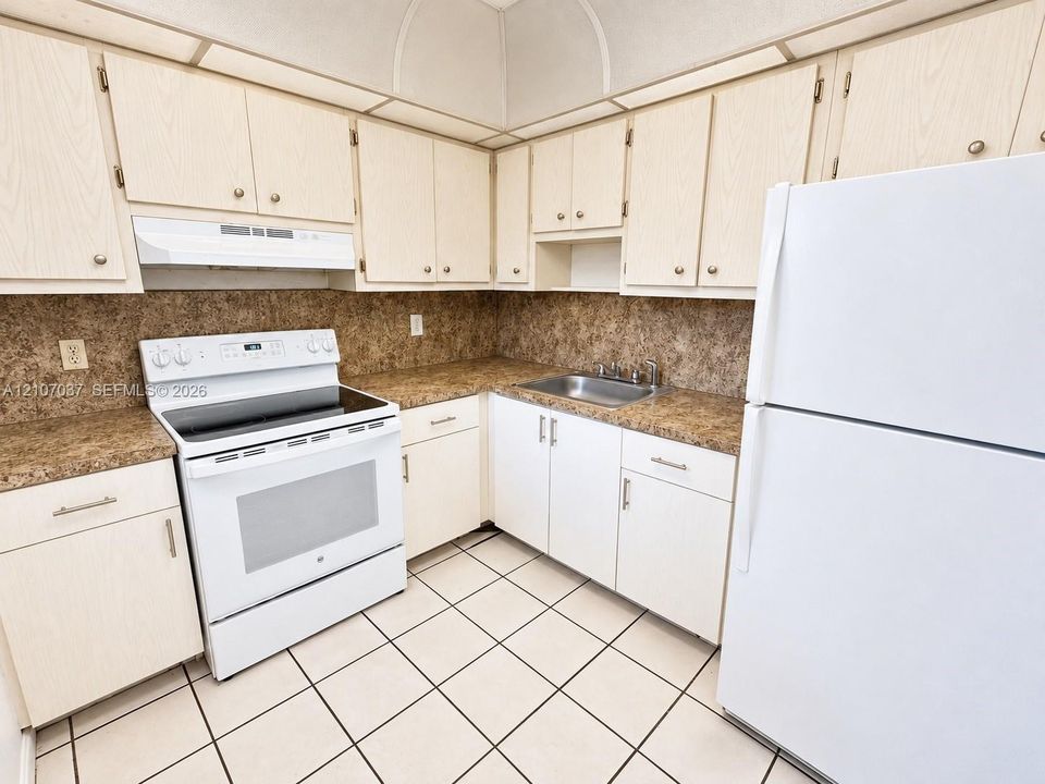 Efficient kitchen layout featuring white cabinetry with ample storage, ceramic tile flooring, stone-finish backsplash, and white appliances including electric range, refrigerator, and dishwasher