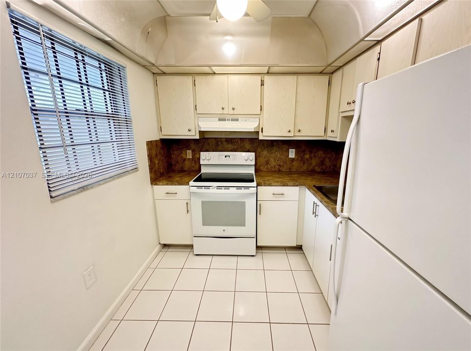 Kitchen featuring light-toned cabinetry, laminate countertops, a white freestanding range, a white refrigerator, and ceramic tile flooring