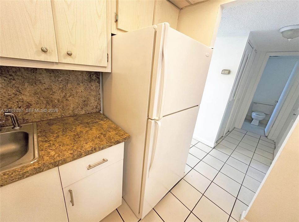 Kitchen area featuring white cabinetry, textured countertops, integrated stainless steel sink with metal faucet, and full-size white refrigerator, with tile flooring throughout