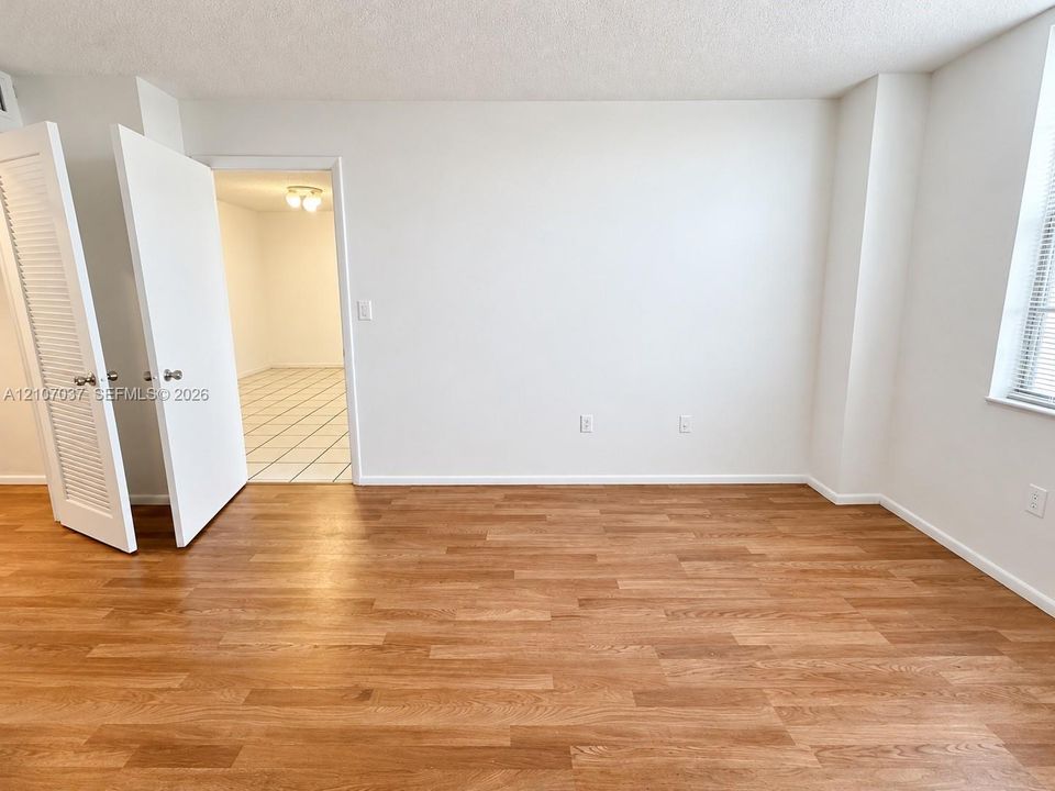 Interior room featuring wood-finish flooring, white walls, louvered closet doors, and large windows with horizontal blinds