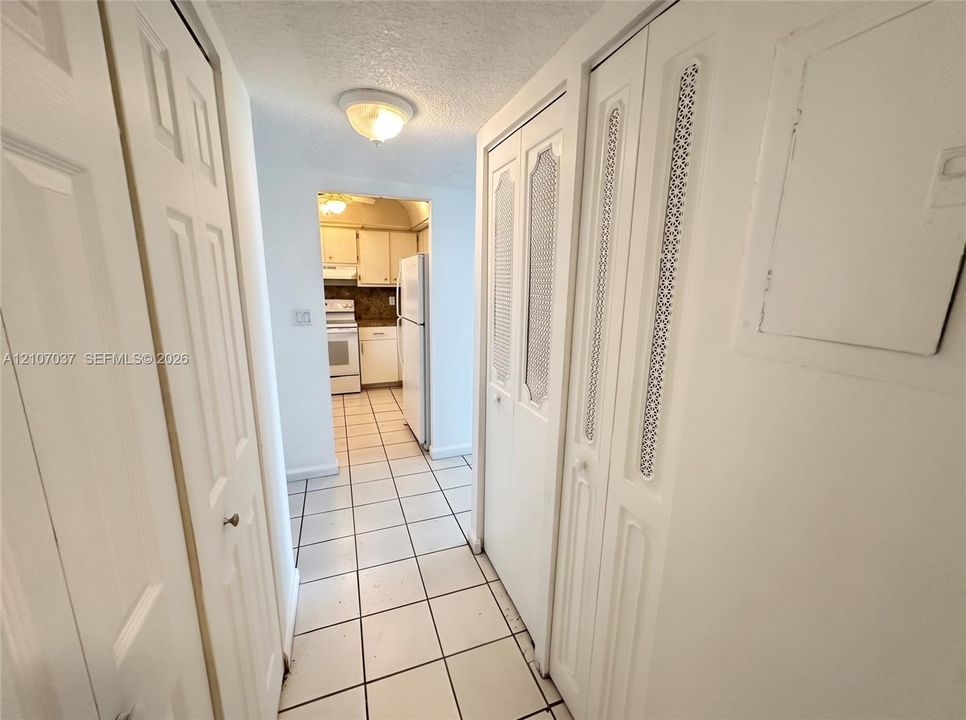 Hallway featuring dual sets of floor-to-ceiling bi-fold closet doors with decorative metal mesh paneling, white ceramic tile flooring, and a flush-mount ceiling fixture