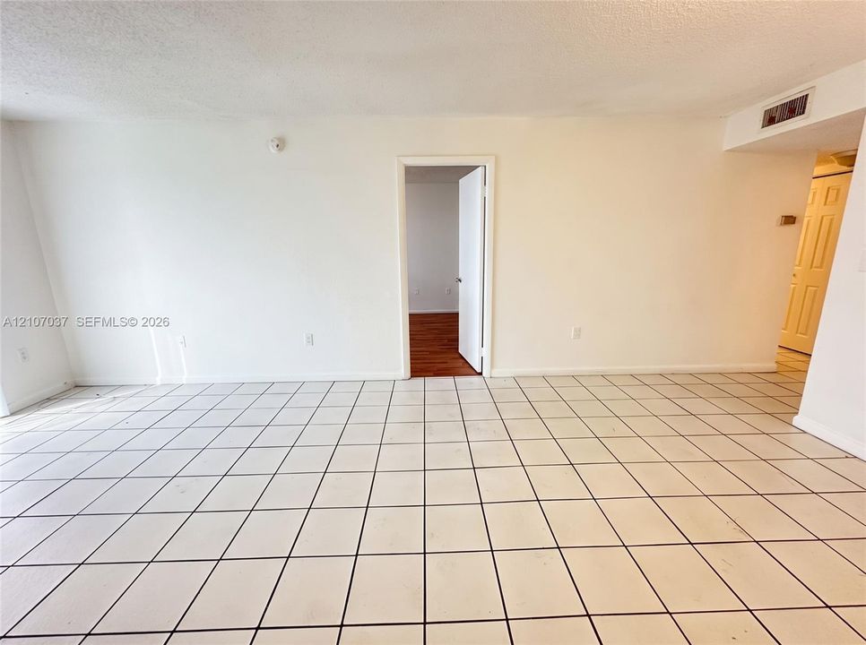 Interior space featuring light-colored ceramic tile flooring, smooth white wall finishes, and a wood-finish floor in the secondary room