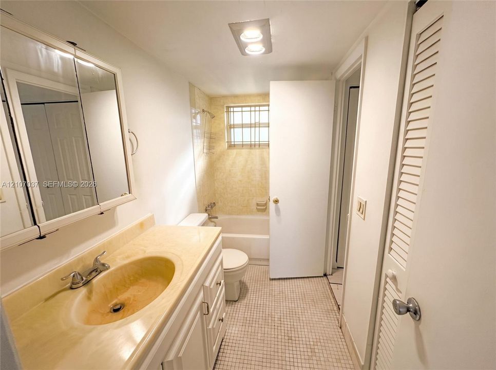 Bathroom featuring a vanity with an integrated sink and countertop, mirrored medicine cabinet, grid-patterned tile flooring, a shower-tub combination, and louvered closet doors
