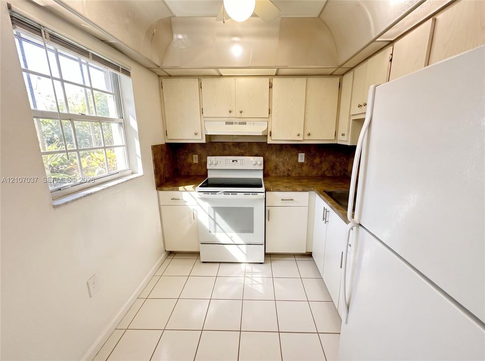 Kitchen featuring light-toned cabinetry, solid surface countertops, tiled flooring, a white electric range, and a window with natural lighting