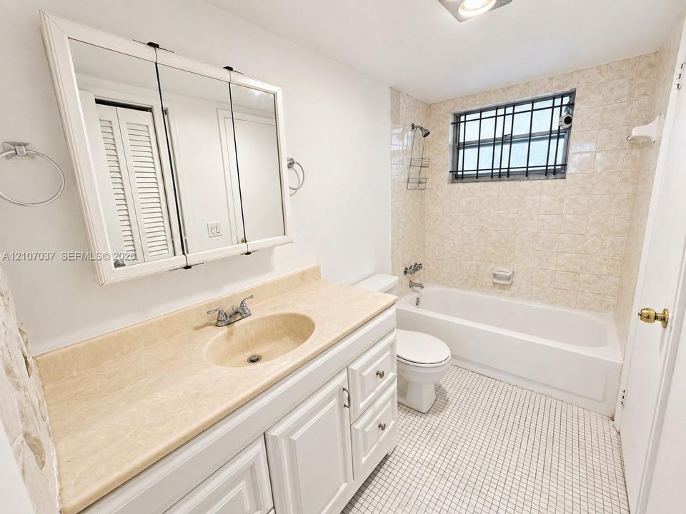 Bathroom featuring a vanity with integrated sink and stone-finish countertop, tri-fold medicine cabinet, white-finish cabinetry, and a bathtub enclosure with tile surround