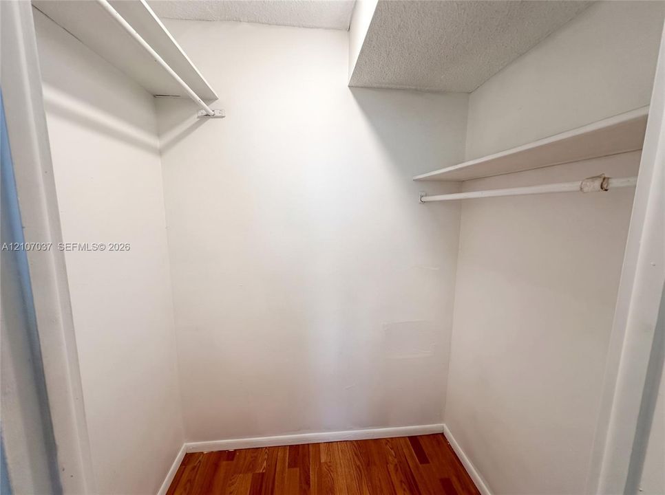 Reach-in closet featuring wood-finish flooring and dual tiers of built-in shelving with integrated rods