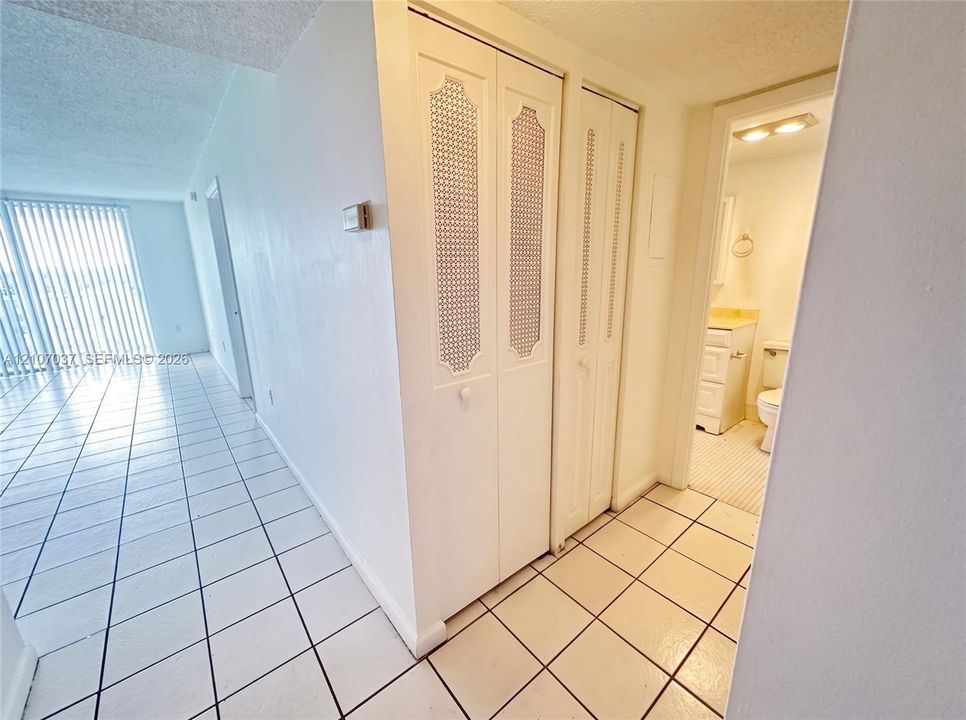 Ceramic tile flooring, dual bi-fold closet doors with decorative latticework panels, and vertical window blinds