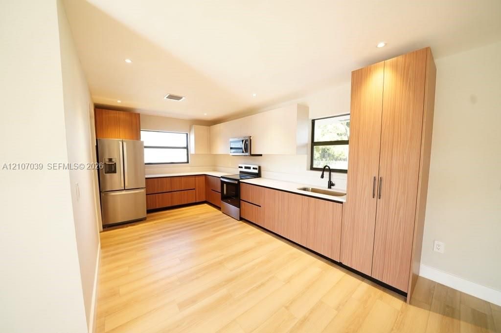 Kitchen featuring two-tone cabinetry with wood-finish lower units and pantry, white upper cabinetry, stainless steel appliances, solid-surface countertops, and wood-finish flooring
