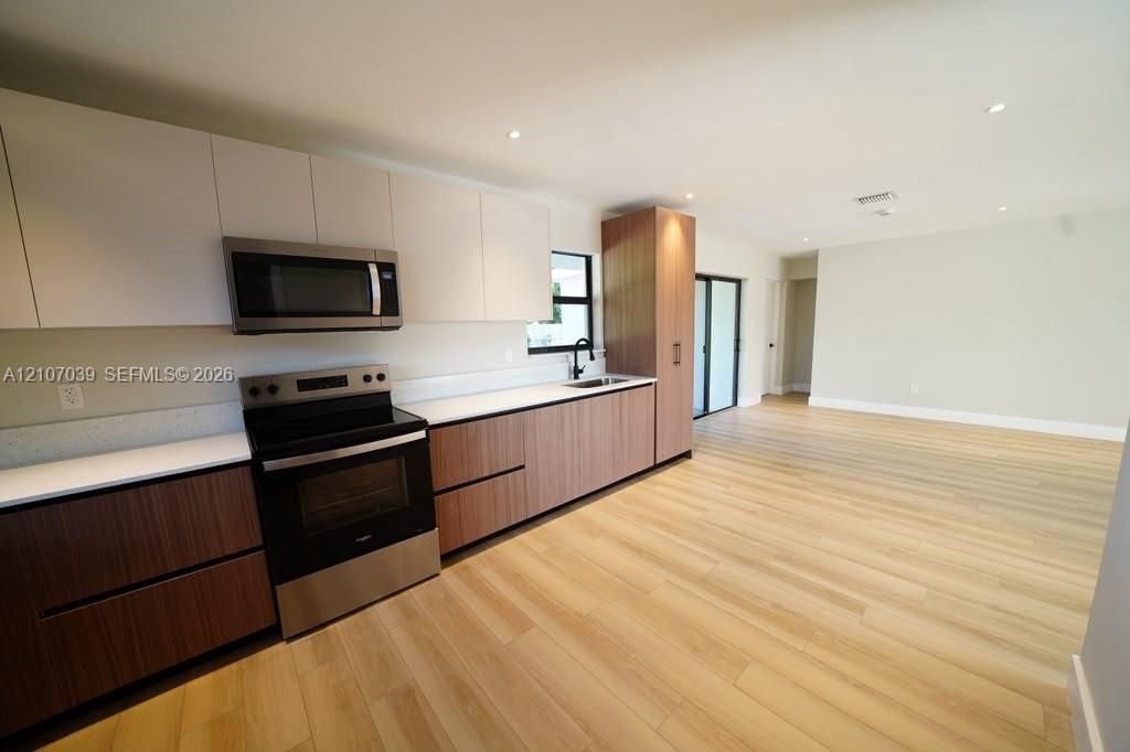 Kitchen featuring dual-toned flat-panel cabinetry, quartz countertops, stainless steel appliances, and wood-finish flooring