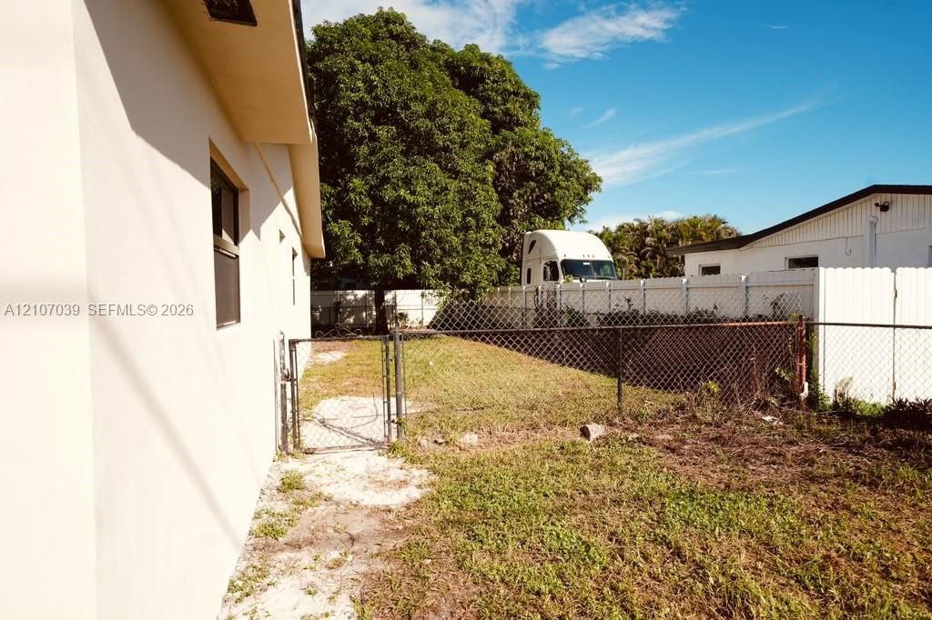 Side yard featuring a chain-link fence, gated entry, and mature trees