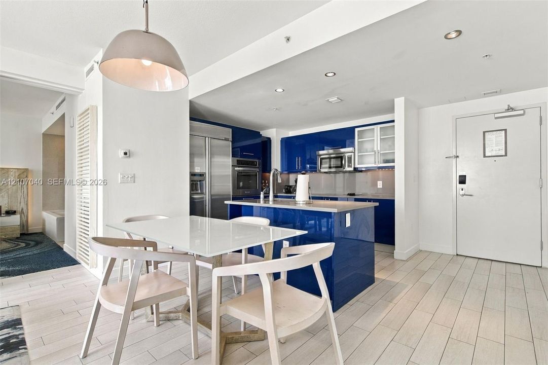 Kitchen featuring high-gloss blue cabinetry, stone-finish countertops, stainless steel appliances, recessed ceiling lighting, and tile flooring