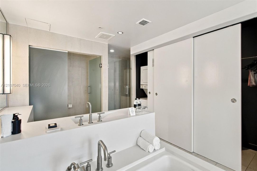 Modern bathroom featuring a rectangular vessel sink with a bridge-style faucet, white solid-surface countertop, walk-in glass shower enclosure, and sliding panel doors