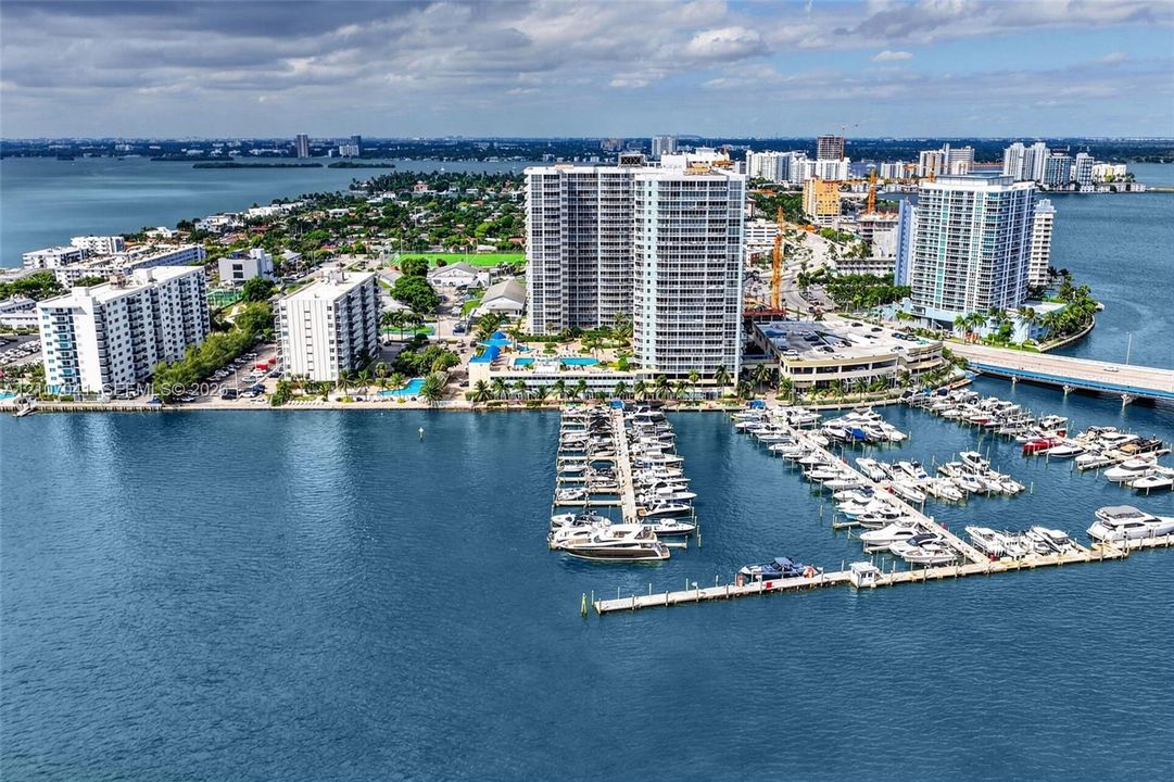 Aerial perspective of a coastal development featuring multi-story residential towers, a private deep-water marina with boat slips, waterfront access, and surrounding bay waters