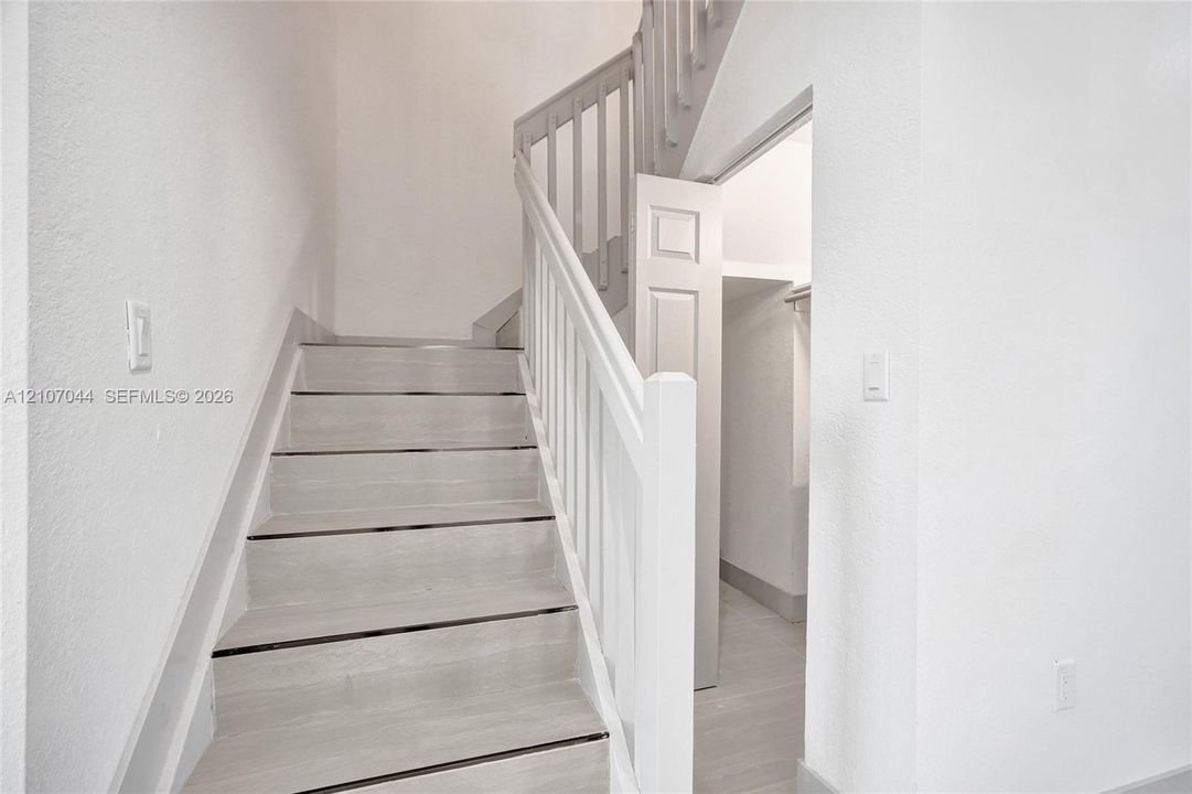 Staircase featuring wood-finish treads, white painted railing, and an integrated storage closet