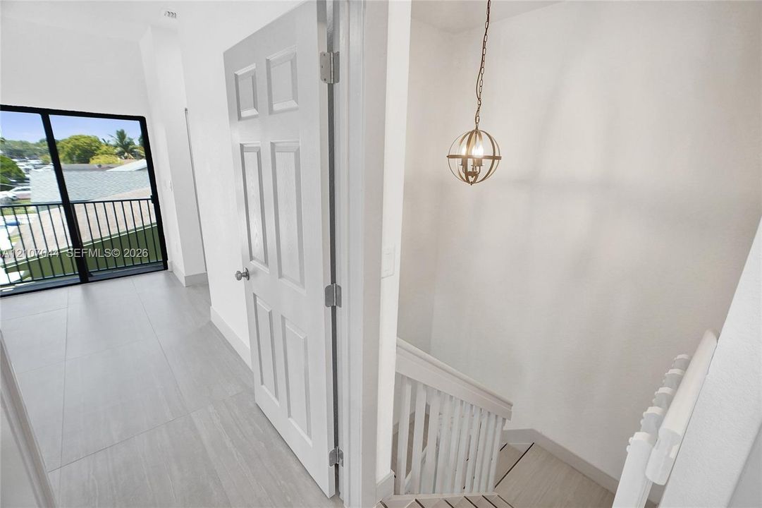 Large-format tile flooring, six-panel interior door, wrought-iron style balcony railing, spherical metal pendant lighting, and wooden staircase with white balusters