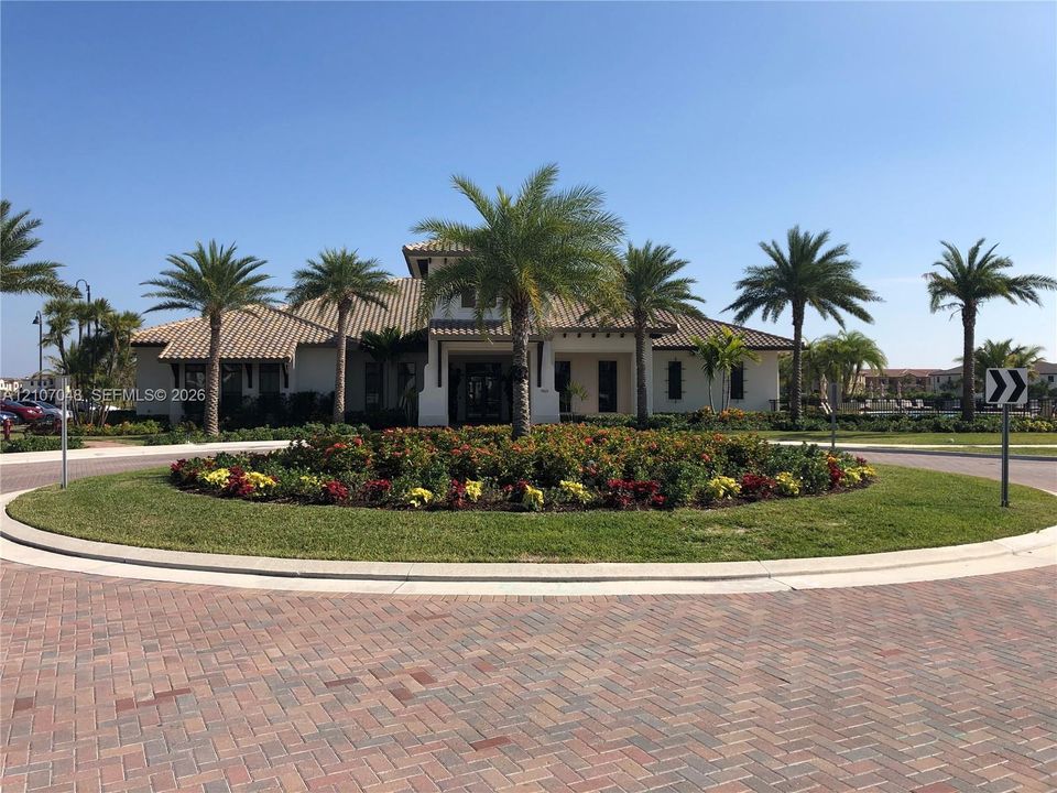 Stucco exterior featuring a multi-hipped tile roof, circular paver driveway, and mature palm tree landscaping