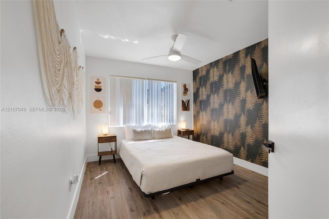 Wood-finish flooring, patterned accent wall, and ceiling fan with integrated lighting
