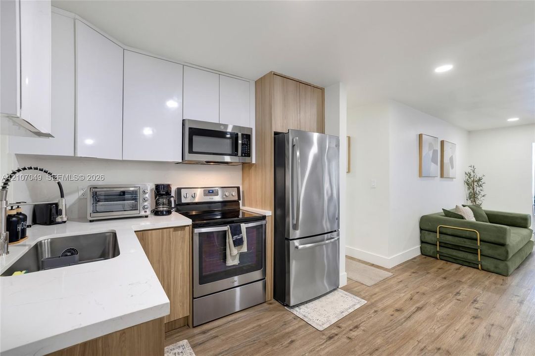Kitchen featuring white upper cabinetry, wood-finish lower cabinetry, quartz countertops, stainless steel appliances, and wood-finish flooring
