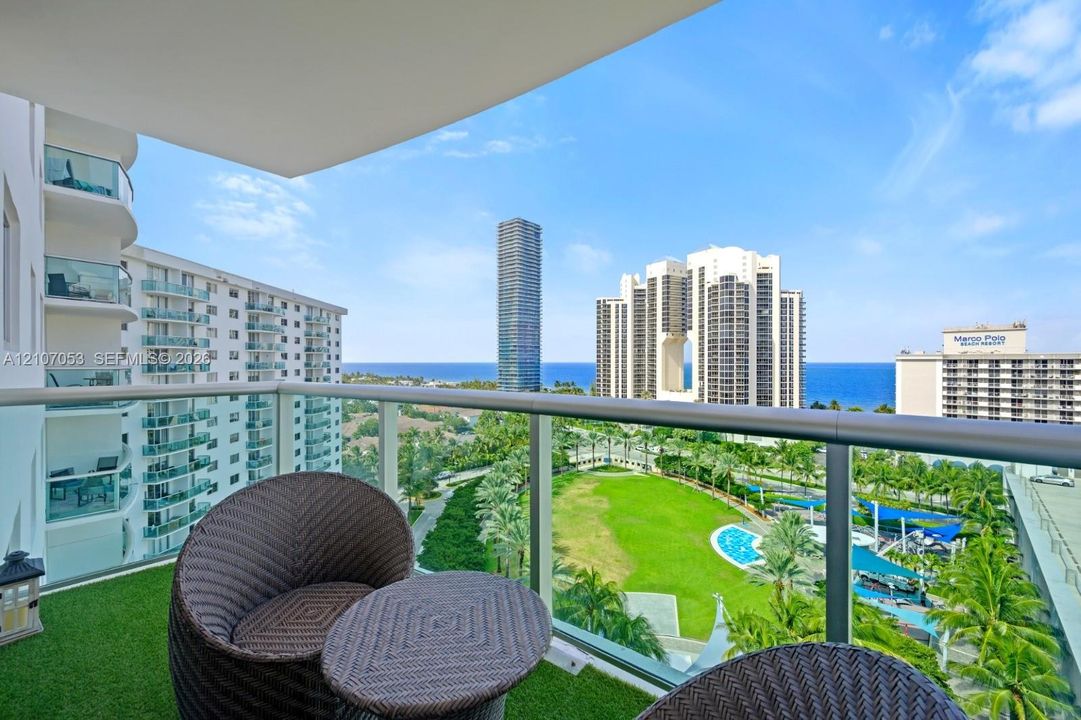 Private balcony featuring glass panel railings and synthetic turf flooring with panoramic coastal and urban scenery