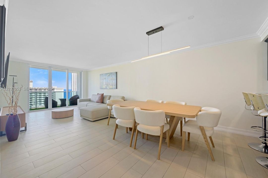 Open-concept living space featuring wood-finish flooring, linear pendant lighting, crown molding, and floor-to-ceiling sliding glass doors