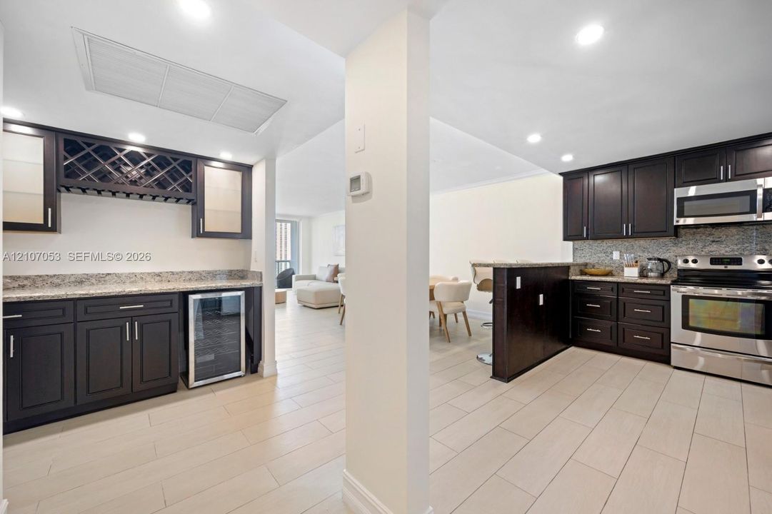 Kitchen featuring dark wood cabinetry, stone countertops, stainless steel appliances, built-in wine cooler, and tile flooring