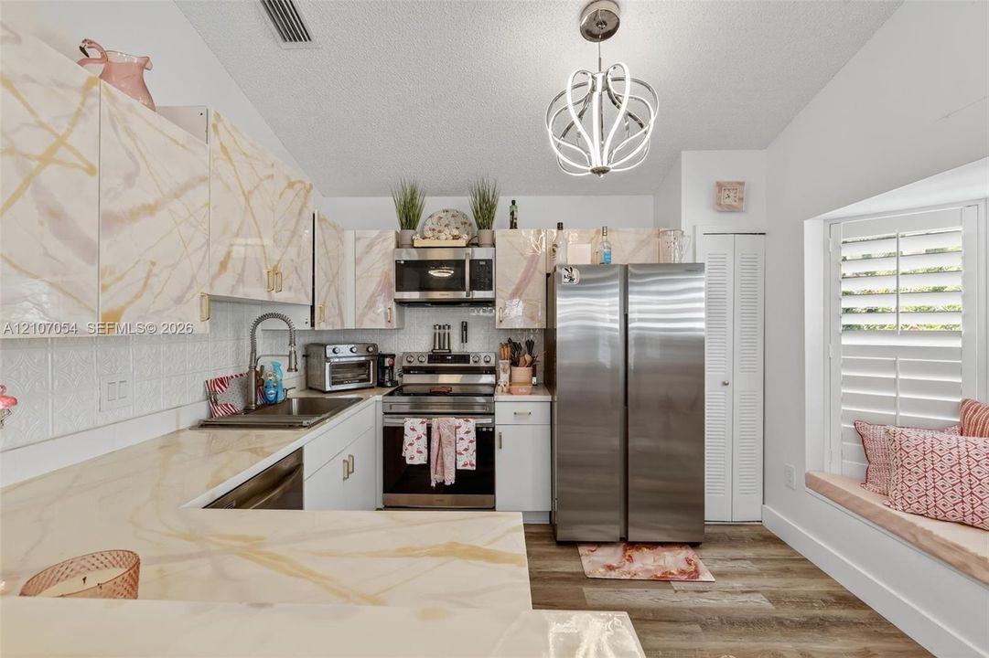 Kitchen featuring patterned cabinetry, granite countertops, stainless steel appliances, laminate flooring, and a built-in window seat with plantation shutters