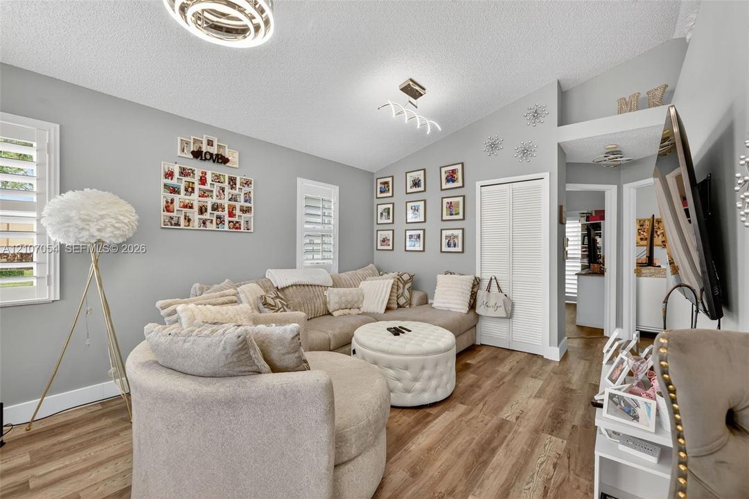 Vaulted ceilings with contemporary light fixtures, laminate flooring, and white louvered window shutters