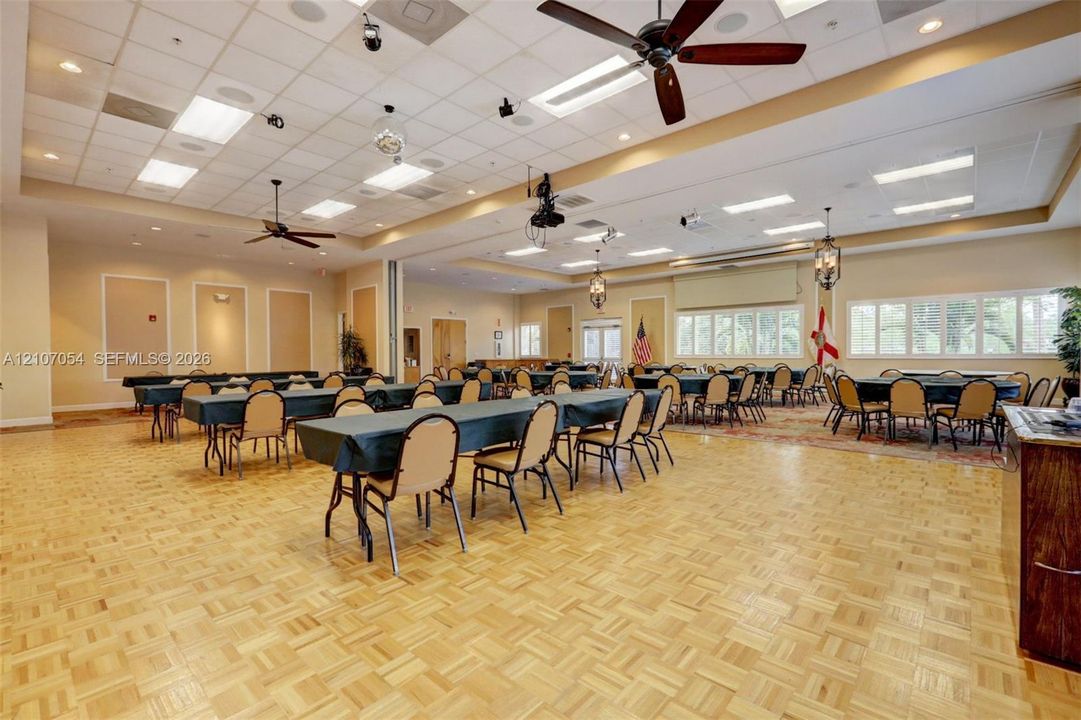 Clubhouse featuring expansive hall featuring parquet wood-finish flooring, a coffered ceiling with recessed lighting, multiple ceiling fans, and large paneled windows