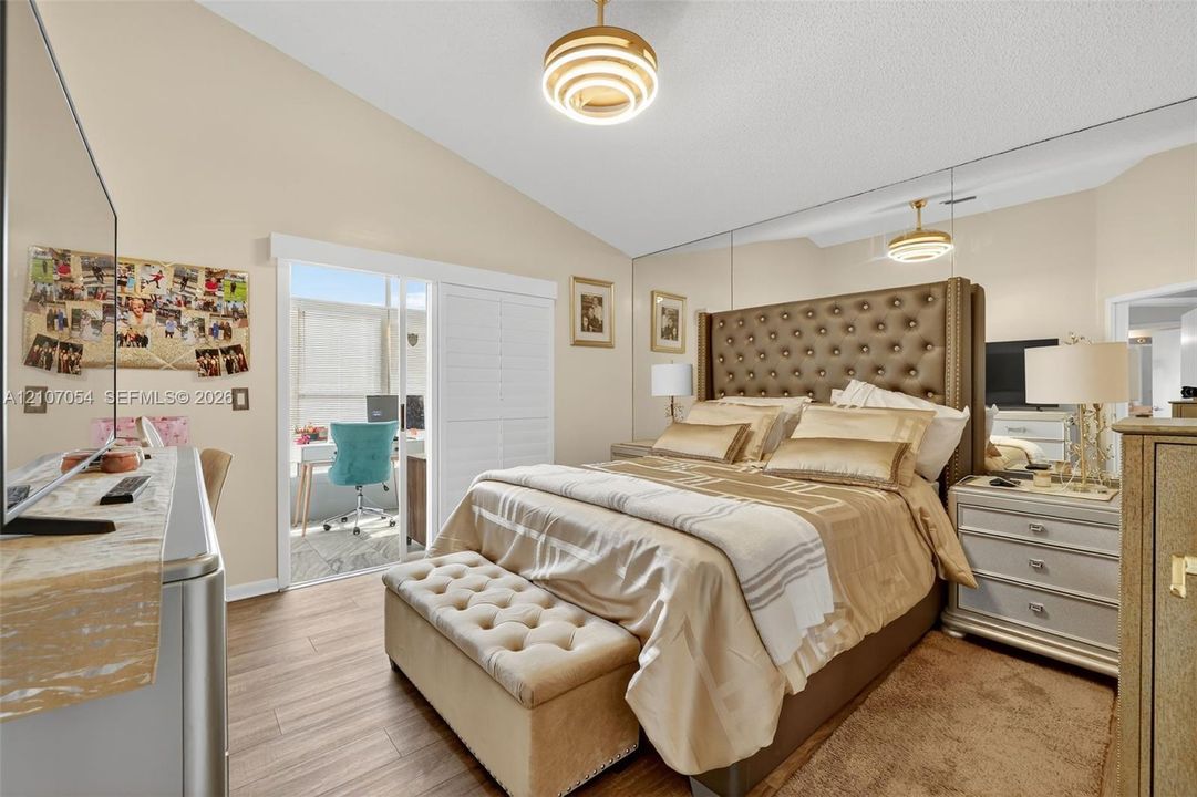 Vaulted ceilings, laminate flooring, full-wall mirrored accent, tiered pendant lighting, and sliding glass door leading to the Florida Room