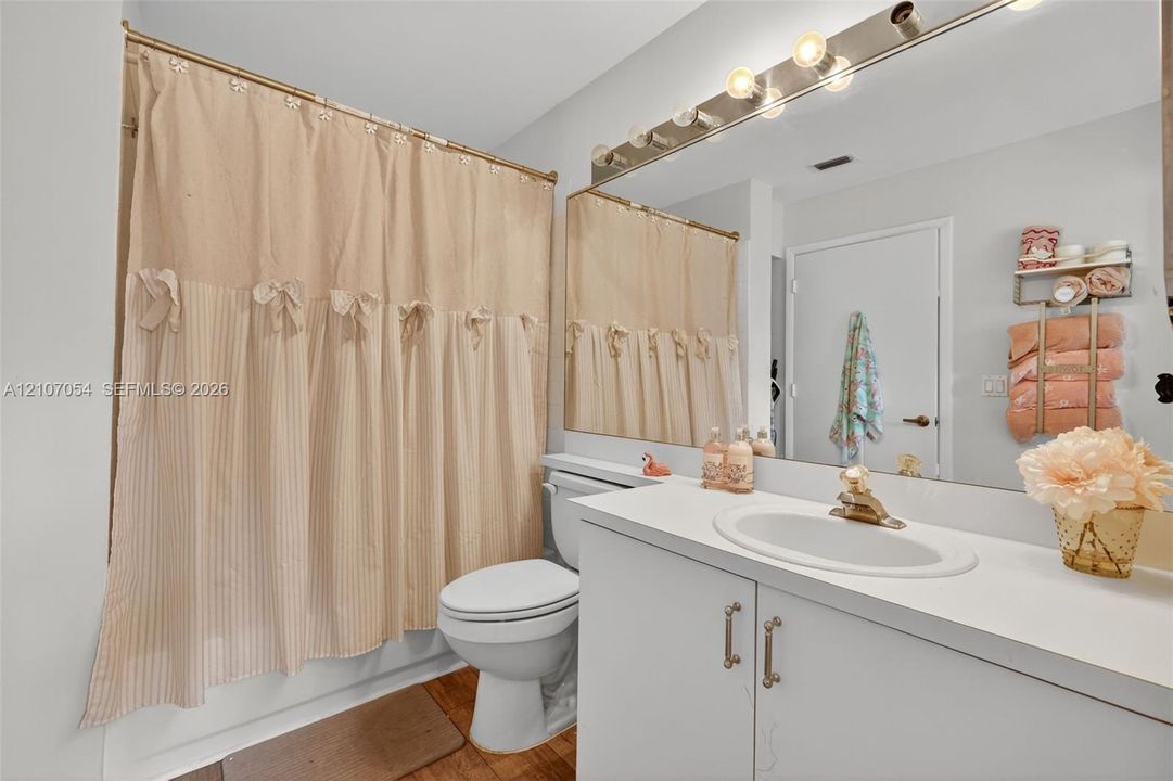 Bathroom featuring a white vanity cabinet, solid-surface countertop with an integrated oval sink, full-width wall-mounted mirror, and multi-bulb strip lighting