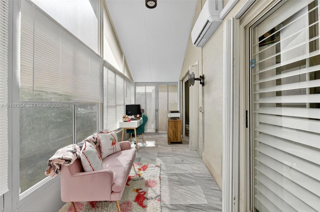 Florida Room featuring stone-finish tile flooring, wall-mounted ductless climate control system, floor-to-ceiling windows with integrated blinds