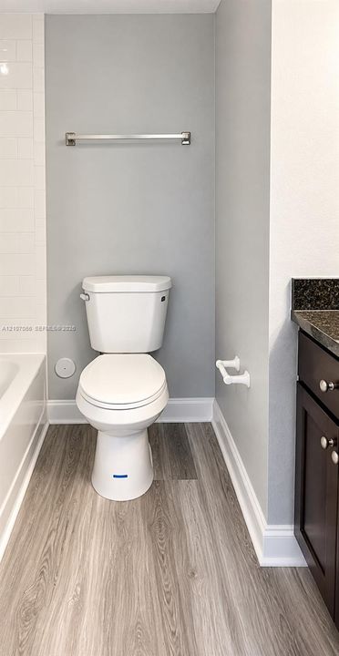 Bathroom featuring wood-finish flooring, a dark-toned vanity with stone-surfaced countertop, a white porcelain toilet, and white wall tile surround