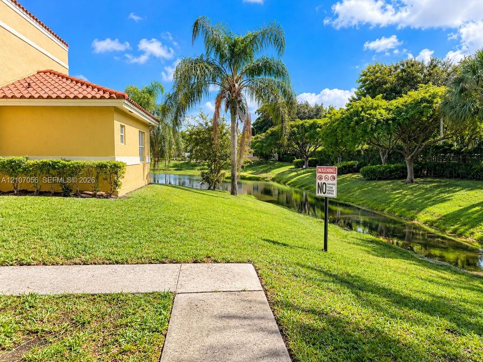 Stucco exterior with a clay tile roof, concrete walkway, and water frontage featuring mature landscaping