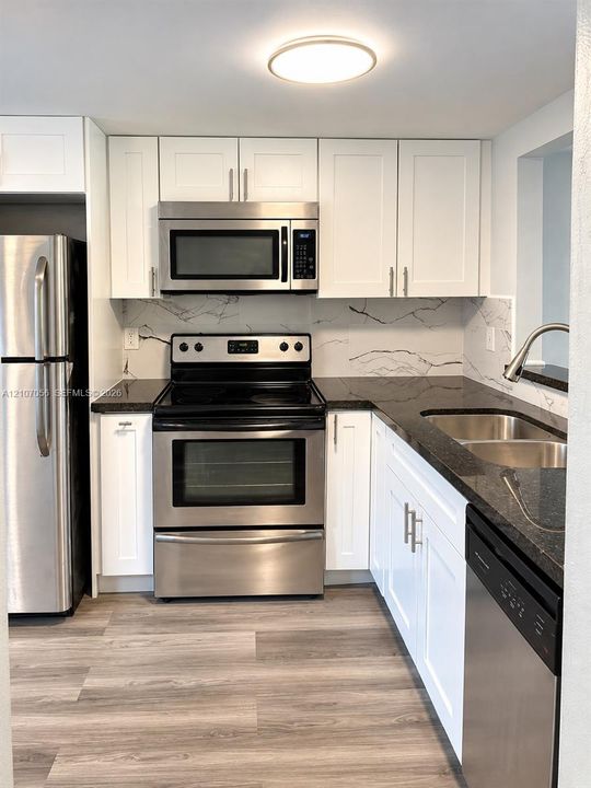 Kitchen featuring white shaker-style cabinetry, dark stone-finish countertops, stainless steel appliances, patterned backsplash, and wood-finish flooring