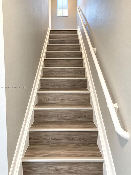 Staircase featuring wood-finish treads, white painted handrails, and neutral wall tones