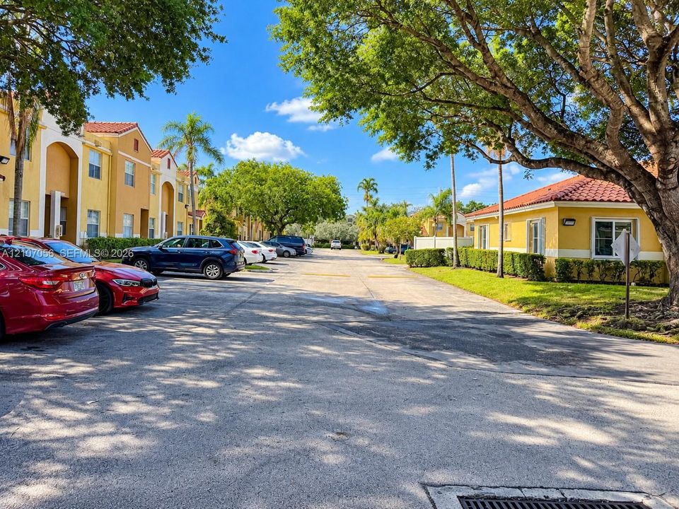 Multi-story stucco buildings featuring clay tile roofs, surface parking, and mature trees