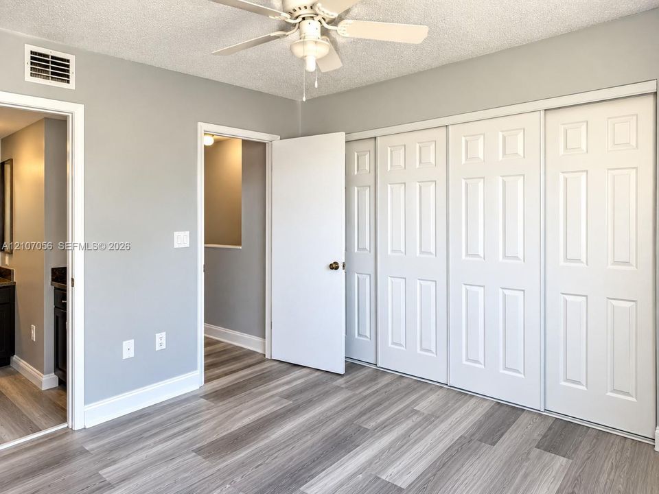Room featuring wood-finish flooring, a white ceiling fan with integrated lighting, and a multi-panel sliding closet