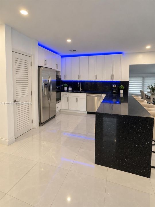 Kitchen featuring white flat-panel cabinetry, dark stone countertops with integrated waterfall edge, stainless steel appliances, recessed ceiling lighting, and large-format porcelain tile flooring