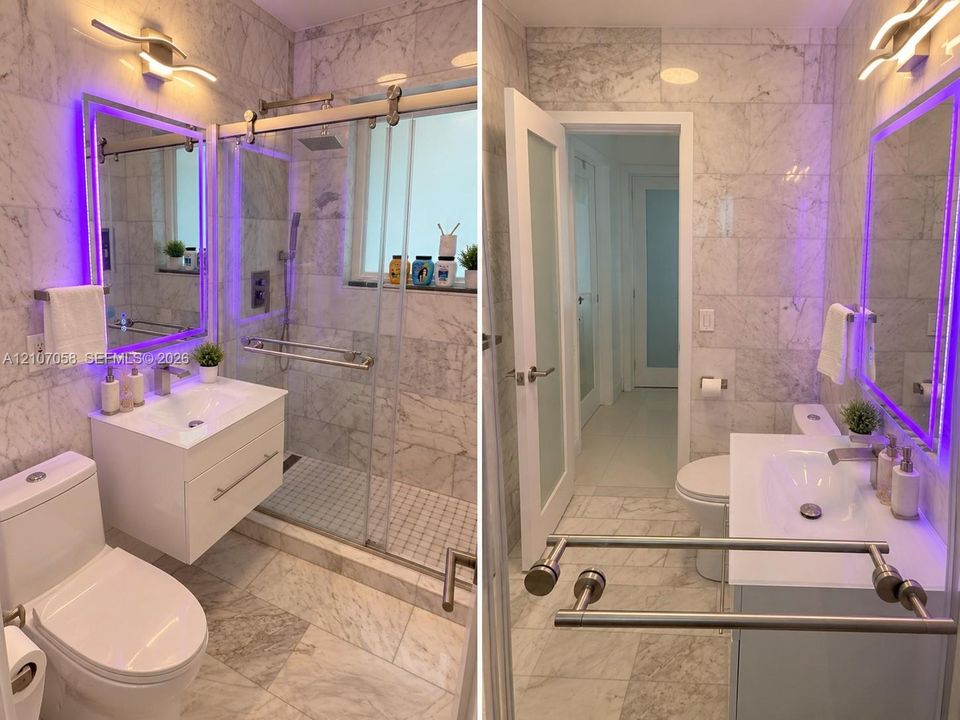 Bathroom featuring floor-to-ceiling stone tile, a modern floating vanity with a white countertop, a walk-in shower with a sliding glass door, and integrated LED vanity lighting