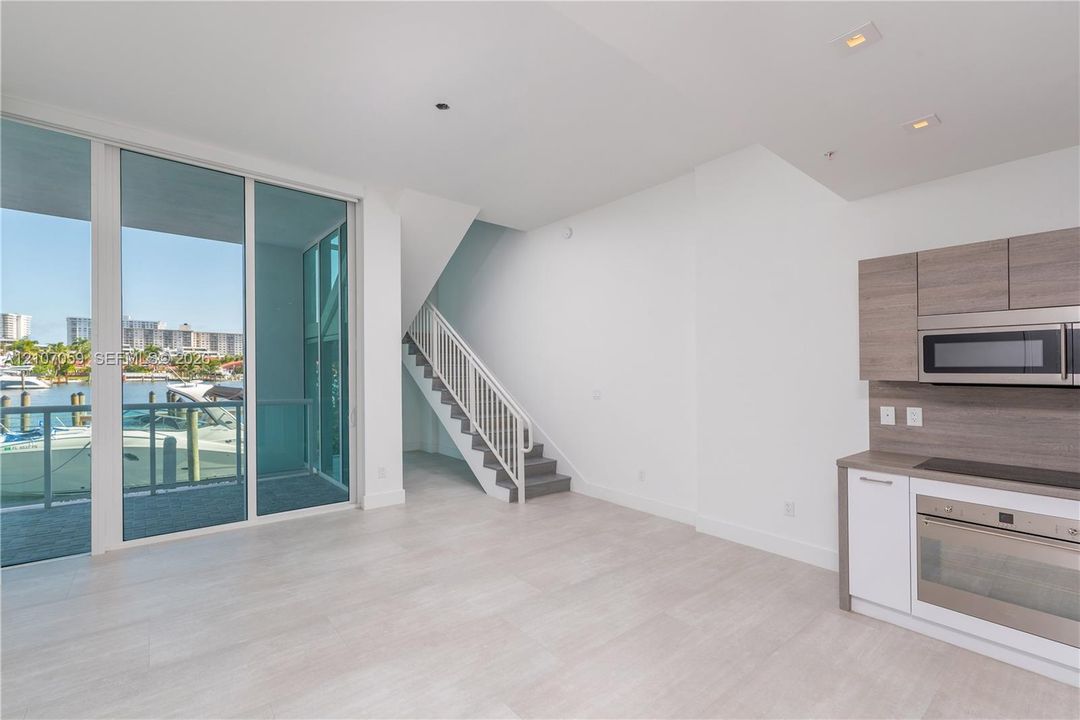 Floor-to-ceiling glass sliding doors, wood-finish cabinetry, built-in stainless steel appliances, recessed ceiling lighting, and a staircase with a metal railing