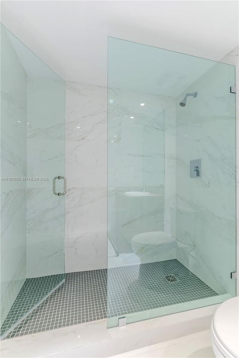 Walk-in shower featuring a frameless glass enclosure, floor-to-ceiling stone-style wall tile, dark mosaic tile flooring, and a wall-mounted shower head