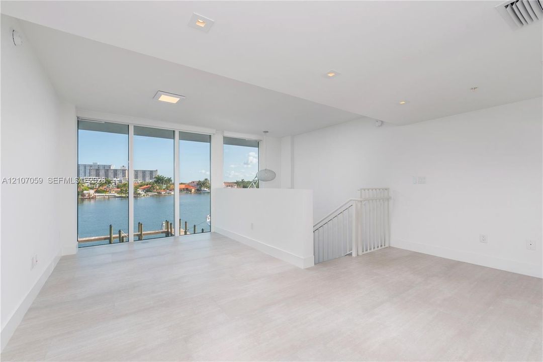Open-concept interior featuring light wood-finish flooring, floor-to-ceiling windows, recessed lighting, and white railings