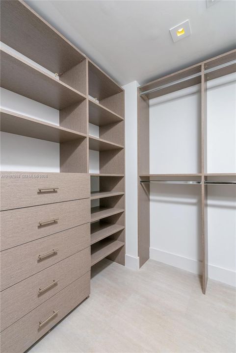 Custom walk-in closet featuring floor-to-ceiling wooden cabinetry, built-in drawer units, adjustable shelving, and integrated metal clothing rods