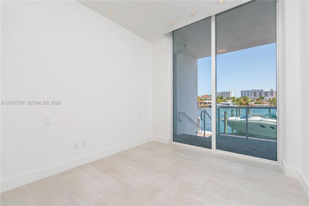 Floor-to-ceiling sliding glass doors, light-toned tile flooring, recessed ceiling lighting, and a private balcony with water-front access
