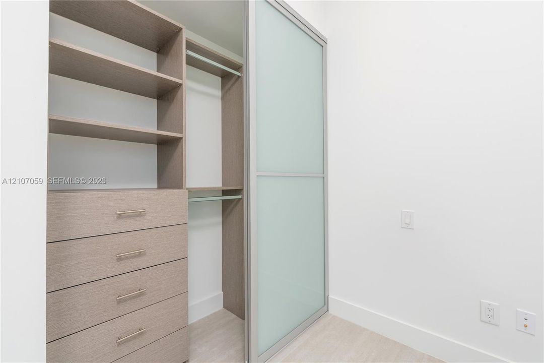 Built-in closet organization system featuring wood-finish cabinetry, open shelving, integrated hanging rods, and frosted glass sliding panels